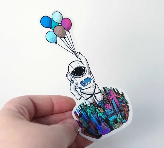 A holographic sticker featuring an astronaut joyfully holding balloons in the air.