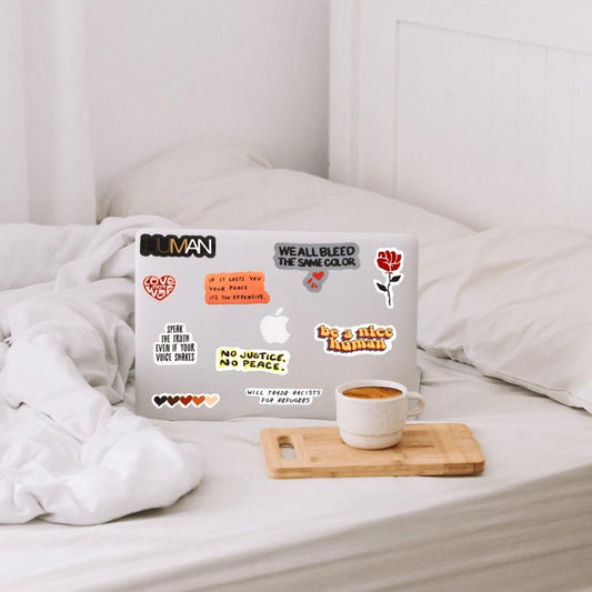 Show your compassion with "Be A Nice Human" sticker. Sticker showcased on laptop on top of white bedding.